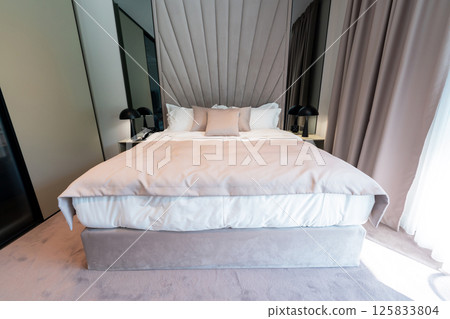 A spacious modern hotel bedroom with cozy bed, soft pillows and elegant interior decor A spacious modern hotel bedroom with cozy bed, soft pillows and elegant interior decor 125833804