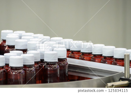 The dark red medicine bottles on the conveyor belt between filling process. 125834115