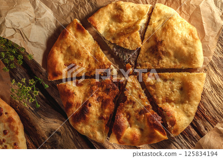 A traditional khachapuri  basking in sunny light against a rustic wooden background, highlighting its golden crust and gooey cheese filling. 125834194