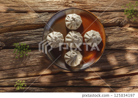Freshly made uncooked handmade khinkali, the traditional Georgian dumplings, in bright sunlight, showcasing fresh ingredients and the art of cooking in action. 125834197