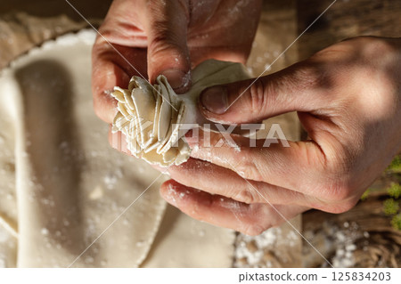 Hands expertly mold khinkali, the traditional Georgian dumplings, in bright sunlight, showcasing fresh ingredients and the art of cooking in action. 125834203