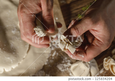 Hands expertly mold khinkali, the traditional Georgian dumplings, in bright sunlight, showcasing fresh ingredients and the art of cooking in action. 125834204