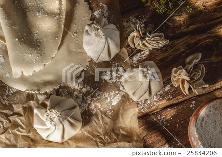Freshly made uncooked handmade khinkali, the traditional Georgian dumplings, in bright sunlight, showcasing fresh ingredients and the art of cooking in action. 125834206