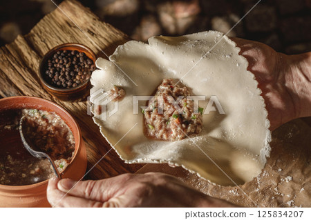 Hands expertly mold khinkali, the traditional Georgian dumplings, in bright sunlight, showcasing fresh ingredients and the art of cooking in action. 125834207
