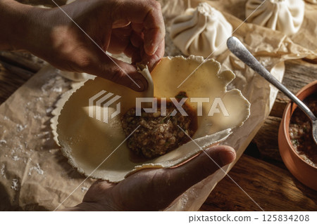 Hands expertly mold khinkali, the traditional Georgian dumplings, in bright sunlight, showcasing fresh ingredients and the art of cooking in action. Hands expertly mold khinkali, the traditional Georgian dumplings, in bright sunlight, showcasing fresh ingredients and the art of cooking in action. 125834208