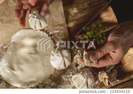 Hands expertly mold khinkali, the traditional Georgian dumplings, in bright sunlight, showcasing fresh ingredients and the art of cooking in action. 125834210