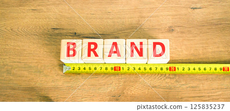 Brand symbol. Concept word Brand on beautiful wooden blocks. Beautiful wooden table wooden background. Beautiful yellow ruler. Business brand concept. Copy space. 125835237