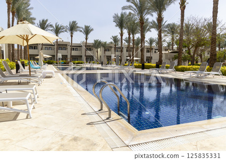 Summer seaside relax mood travel vacation a luxurious pool hotel interior for a summer holiday in warm countries. Beautiful tropical beach hotel resort with swimming pool, sun loungers palm trees Summer seaside relax mood travel vacation a luxurious pool hotel interior for a summer holiday in warm countries. Beautiful tropical beach hotel resort with swimming pool, sun loungers palm trees 125835331