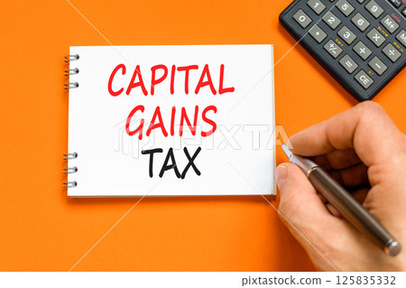 Capital gains tax symbol. Concept words Capital gains tax on beautiful white note. Beautiful orange background. Businessman hand. Business and capital gains tax concept. Copy space. Capital gains tax symbol. Concept words Capital gains tax on beautiful white note. Beautiful orange background. Businessman hand. Business and capital gains tax concept. Copy space. 125835332