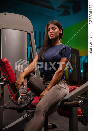 fit individual poses confidently on gym equipment while focusing on strength training exercises. colorful backdrop adds energy workout environment highlighting dedication fitness. 125836135