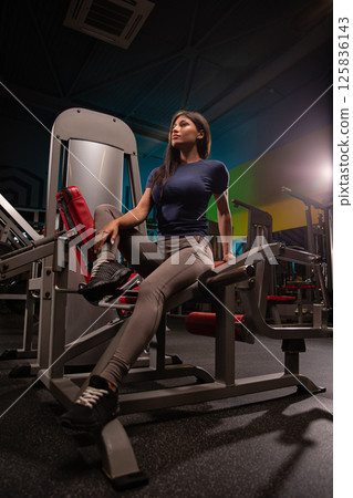 fitness enthusiast performs strength training on gym equipment in well lit environment during evening. individual showcases focus and determination while exercising. fitness enthusiast performs strength training on gym equipment in well lit environment during evening. individual showcases focus and determination while exercising. 125836143