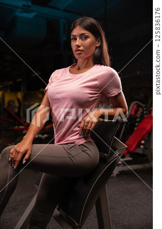 fitness model poses confidently on chair in well equipped gym. dynamic lighting emphasizes her strength and functionality of athletic wear she showcases. 125836176