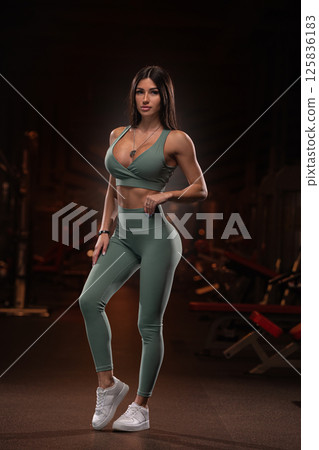 gym setting fitness model stands poise while wearing form fitting athletic wear. confident pose highlights her toned physique and dedication fitness during workout. 125836183