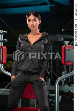 fitness model stands poised in modern gym dressed in stylish black workout outfit. environment is vibrant exercise equipment emphasizing active lifestyle and dedication fitness. fitness model stands poised in modern gym dressed in stylish black workout outfit. environment is vibrant exercise equipment emphasizing active lifestyle and dedication fitness. 125836317