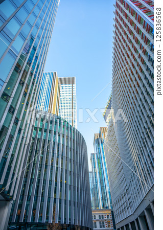 Skyscrapers dominate the urban landscape of London City, reflecting a mix of contemporary architecture under a clear blue sky. The sharp lines and glass facades create a striking visual experience. 125836568