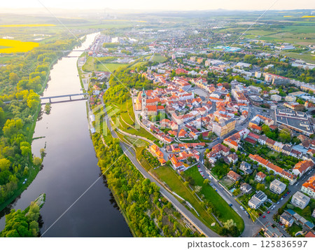 Melnik city is beautifully captured from above, showcasing its historic chateau overlooking the winding Labe River. The vibrant landscape highlights the blend of nature and architecture. 125836597
