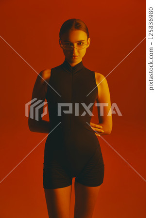 Portrait of confident and stylish young woman in black jumpsuit and trendy glasses, posing with intense gaze in camera Portrait of confident and stylish young woman in black jumpsuit and trendy glasses, posing with intense gaze in camera 125836980