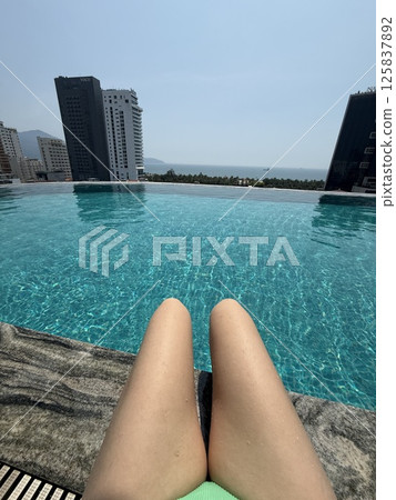 unrecognizable girl knees Poolside city view Woman relaxing by luxury hotel pool with city skyline. Leisure and travel. unrecognizable girl knees Poolside city view Woman relaxing by luxury hotel pool with city skyline. Leisure and travel. 125837892