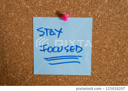 Light blue sticky note on cork board saying stay focused Light blue sticky note on cork board saying stay focused 125838207