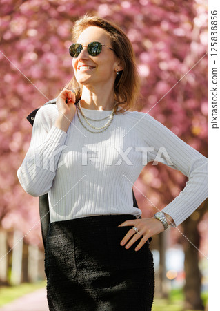 Portrait scenic young adult pretty happy woman enjoy walking spring city street blooming pink cherry trees alley background in Magdeburg city. Female person joyful carefree smiling outdoors Portrait scenic young adult pretty happy woman enjoy walking spring city street blooming pink cherry trees alley background in Magdeburg city. Female person joyful carefree smiling outdoors 125838856