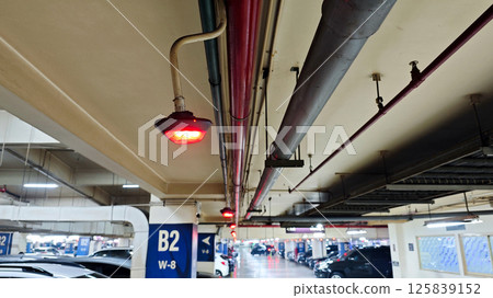 Red Parking Spot Indicator Light in Basement Car Parking Area with Exposed Pipes and Ceiling Fixtures 125839152