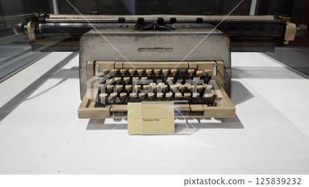 Vintage Retro Typewriter with Beige Keys and Metal Frame on Display in Glass Case at Museum Exhibit 125839232