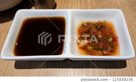 Close-Up of Dual Sauces in White Dish on Wooden Table Featuring Dark Soy Sauce and Spicy Salsa Close-Up of Dual Sauces in White Dish on Wooden Table Featuring Dark Soy Sauce and Spicy Salsa 125839236