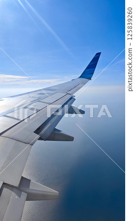 View of Airplane Wing Over Ocean with Clear Blue Sky from Passenger Window on Sunny Day View of Airplane Wing Over Ocean with Clear Blue Sky from Passenger Window on Sunny Day 125839260