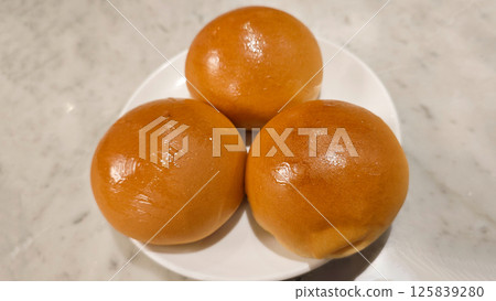 Three Golden Brown Barbecued Pork Buns on a White Plate with a Marble Background in a Restaurant Setting 125839280