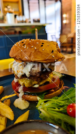 A perfect Gourmet Cheeseburger with Beef Egg and Fries on Blue Plate in Cozy Cafe Setting with Bright Lighting and Wooden Table 125839384