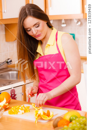 Woman housewife in kitchen cutting orange fruits Woman housewife in kitchen cutting orange fruits 125839489