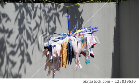 Colorful Hanging Laundry Drying on Blue Rack in Sunny Backyard Against gray Wall 125839630