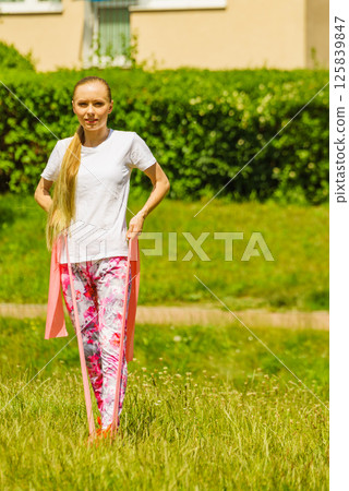 Girl doing exercises outdoor, using resistance fit band. 125839847