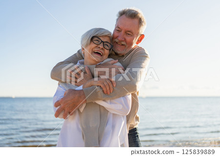 Senior mature couple hugging enjoying outdoor recreation walking on beach. Old husband wife embracing with tenderness love enjoying sweet bonding. Grandmother grandfather together. Family moment love 125839889