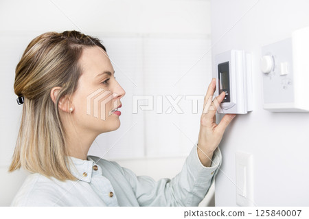 woman set the thermostat at house. 125840007