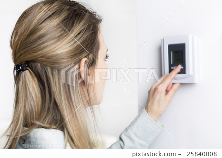 woman set the thermostat at house. 125840008