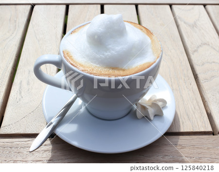 Cappuccino in a white cup with a plate and a dessert spoon. 125840218