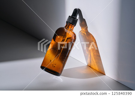 A bottle of serum made of brown glass on a white background with stripe of light. 125840390