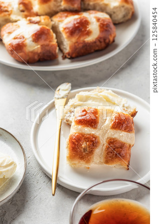 Traditional Easter hot cross buns on white plate with butter on light gray background. Delicious Easter breakfast 125840454
