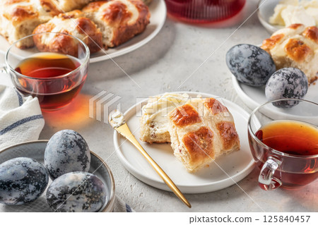 Traditional Easter hot cross buns on white plate with butter, cup of tea and eggs. Delicious Easter breakfast 125840457