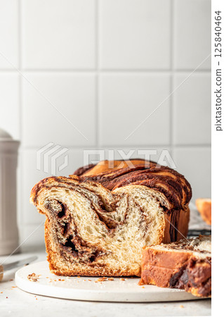Chocolate Babka or Brioche loaf Bread sliced on white kitchen background. Homemade sweet yeast pastry for easter, text space Chocolate Babka or Brioche loaf Bread sliced on white kitchen background. Homemade sweet yeast pastry for easter, text space 125840464