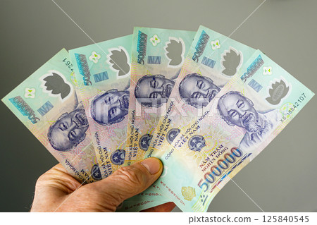 Hand holding five 500,000 dong denominations Vietnamese banknotes on a gray background 125840545