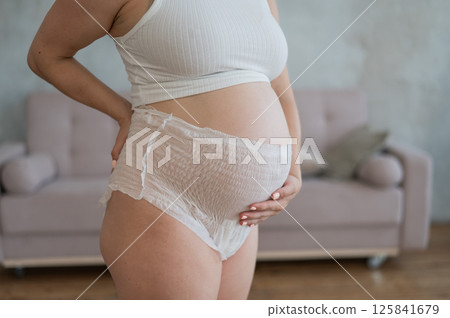 Caucasian pregnant woman in adult diapers suffers from incontinence. Close-up of belly.  125841679