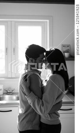 Married couple hugging in the morning in the kitchen. Man and woman in love hugging in the rays of the morning sun. Monochrome image.  125841928