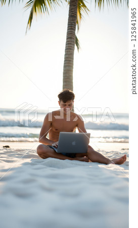 Freelancer guy works remotely on his laptop while sitting on the sand on a tropical beach 125841965