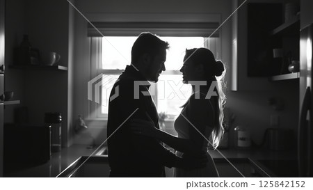 Married couple hugging in the morning in the kitchen. Man and woman in love hugging in the rays of the morning sun. Monochrome image.  125842152