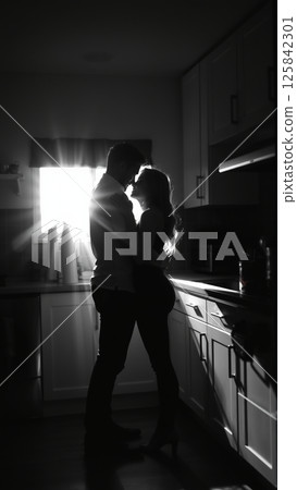 Married couple hugging in the morning in the kitchen. Man and woman in love hugging in the rays of the morning sun. Monochrome image.  125842301