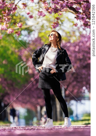 Portrait scenic young adult pretty happy woman enjoy walking spring city street blooming pink cherry trees alley background in Magdeburg city. Female person joyful carefree smiling outdoors Portrait scenic young adult pretty happy woman enjoy walking spring city street blooming pink cherry trees alley background in Magdeburg city. Female person joyful carefree smiling outdoors 125842366