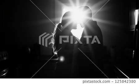 Married couple hugging in the morning in the kitchen. Man and woman in love hugging in the rays of the morning sun. Monochrome image.  125842380