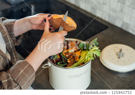 Compost the kitchen waste, recycling at home. Woman putting vegetables cutted leftovers into the garbage, compost bin on the table of kitchen. Environmentally responsible, ecology. Selective focus Compost the kitchen waste, recycling at home. Woman putting vegetables cutted leftovers into the garbage, compost bin on the table of kitchen. Environmentally responsible, ecology. Selective focus 125842752